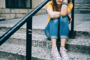 Teen sitting alone on steps, conveying feelings of stress or emotional overwhelm. The words "help" are written in chalk on the steps.